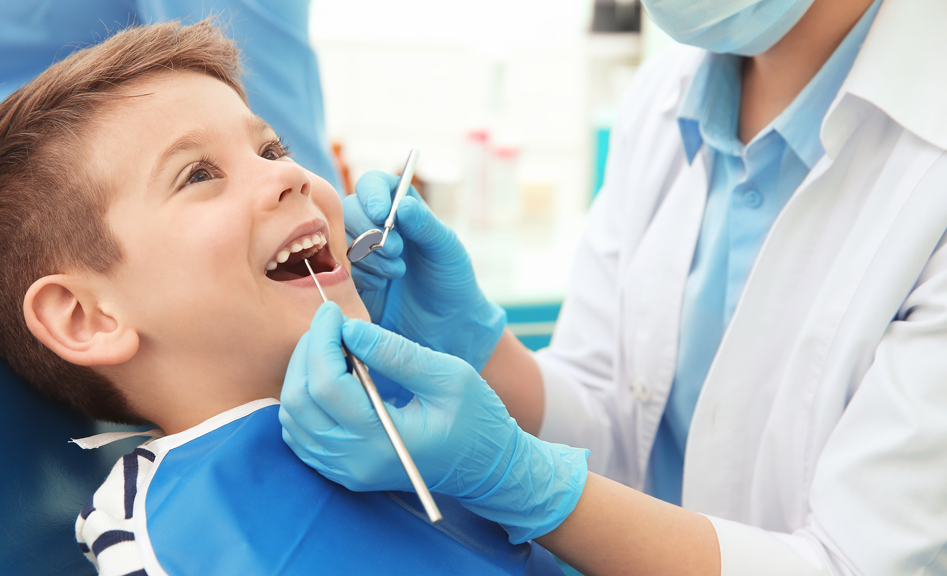 Dentist examining little boy’s teeth in clinic